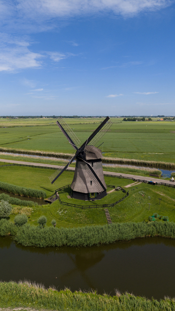 Aerial view of Bovenmolen G windmill surrounded by lush green fields and a canal in Schermerhorn Noord Holland Netherlands. Aerial view of Bovenmolen G windmill surrounded by lush green fields and a canal in Schermerhorn Noord Holland Netherlands.