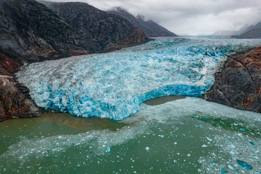 Aerial view of the Mendenhall Glacier with its vibrant blue ice surrounded by rugged mountains and floating icebergs in the glacial lake near Juneau Alaska United States. Aerial view of the Mendenhall Glacier with its vibrant blue ice surrounded by rugged mountains and floating icebergs in the glacial lake near Juneau Alaska United States.