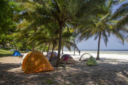 View of colorful camping tents pitched under palm trees on the white sand of Tiwi Beach with the blue ocean in the background Tiwi Wilaya ya Kwale Kenya. View of colorful camping tents pitched under palm trees on the white sand of Tiwi Beach with the blue ocean in the background Tiwi Wilaya ya Kwale Kenya.