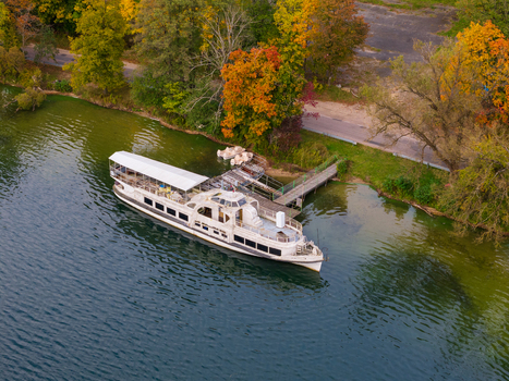 Aerial view of a white tour boat docked at a wooden pier on the calm waters of Galve Lake surrounded by vibrant autumn foliage in Trakai Vilnius County Lithuania. Aerial view of a white tour boat docked at a wooden pier on the calm waters of Galve Lake surrounded by vibrant autumn foliage in Trakai Vilnius County Lithuania.