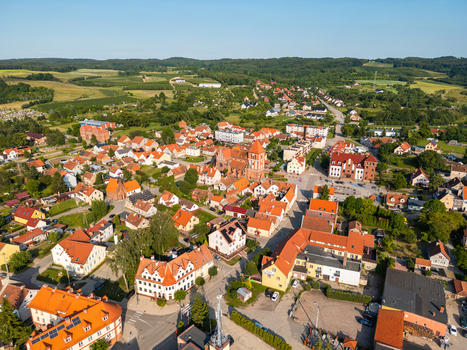Aerial view of a historic town with red tiled rooftops a prominent church and surrounding green fields under a clear blue sky in Tolkmicko Warmian Masurian Voivodeship Poland.