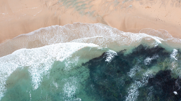 Aerial view of the turquoise waves crashing onto the golden sandy shore of Constantine Bay in Padstow Cornwall United Kingdom. Aerial view of the turquoise waves crashing onto the golden sandy shore of Constantine Bay in Padstow Cornwall United Kingdom.