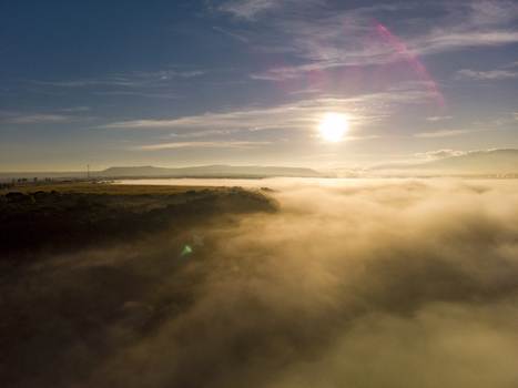 Aerial view of a dense layer of morning fog rolling over the landscape at sunrise with golden light illuminating the clouds and distant hills in Tonala Jalisco Mexico. Aerial view of a dense layer of morning fog rolling over the landscape at sunrise with golden light illuminating the clouds and distant hills in Tonala Jalisco Mexico.