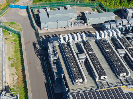 Aerial view of a data center featuring rows of cooling units and server infrastructure within a secure fenced perimeter in the United Kingdom.