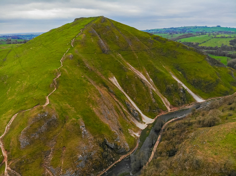 Aerial view of Thorpe Cloud in Dovedale with steep green slopes a winding path to the summit and the River Dove flowing through the valley in Ashbourne England United Kingdom. Aerial view of Thorpe Cloud in Dovedale with steep green slopes a winding path to the summit and the River Dove flowing through the valley in Ashbourne England United Kingdom.