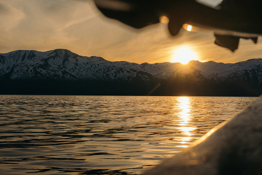 View of golden sunset bathes the tranquil waters as jagged snow capped mountains loom in the background casting long shadows over the serene landscape H&uacute;sav&iacute;k Iceland.