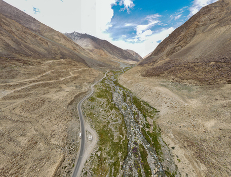 Aerial view of a winding road and a stream flowing through the rugged mountain valley of Ladakh under a bright blue sky in Ladakh Division Ladakh India. Aerial view of a winding road and a stream flowing through the rugged mountain valley of Ladakh under a bright blue sky in Ladakh Division Ladakh India.
