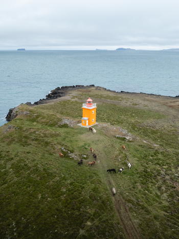 Aerial view of the vibrant yellow lighthouse standing resiliently against the moody blues of the ocean H&uacute;nabygg&eth; Iceland.
