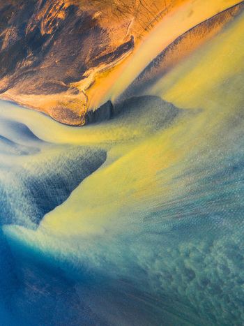 Aerial view of a vibrant glacial river delta with intricate braided channels contrasting yellow sediment and dark volcanic sand patterns in Iceland. Aerial view of a vibrant glacial river delta with intricate braided channels contrasting yellow sediment and dark volcanic sand patterns in Iceland.