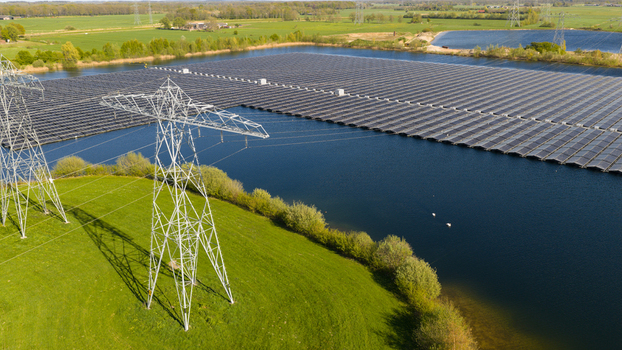 Aerial view of a floating solar farm on a lake with high voltage power pylons and green fields under a clear sky in Zwolle Overijssel Netherlands. Aerial view of a floating solar farm on a lake with high voltage power pylons and green fields under a clear sky in Zwolle Overijssel Netherlands.