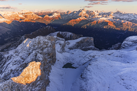 Aerial view of snow dusted Dolomite mountains glow with the warm hues of the setting sun casting shadows across the valleys below Antermoia lake Trentino South Tyrol Italy.