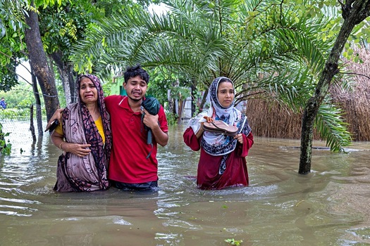 Banshkhali Upazila Chittagong Division Bangladesh 10 July 2026 View of people wading through deep floodwaters in a rural area with a distressed woman crying. Banshkhali Upazila Chittagong Division Bangladesh 10 July 2026 View of people wading through deep floodwaters in a rural area with a distressed woman crying.