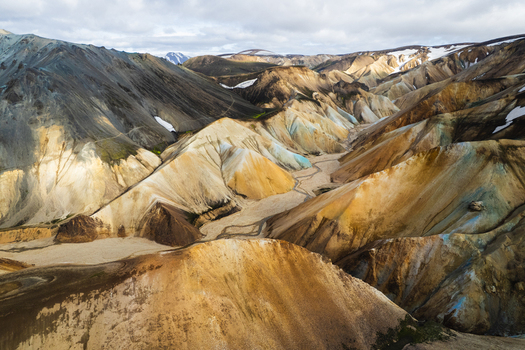 Aerial view of the colorful rhyolite mountains of Landmannalaugar with winding riverbeds and patches of snow under a cloudy sky Rangarthing ytra Iceland. Aerial view of the colorful rhyolite mountains of Landmannalaugar with winding riverbeds and patches of snow under a cloudy sky Rangarthing ytra Iceland.