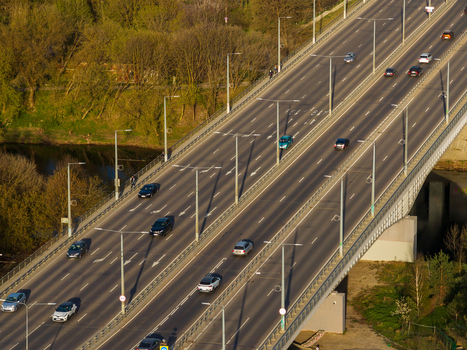 Aerial view of a multi lane bridge with cars driving over a river surrounded by lush green trees in warm sunlight Vilnius County Lithuania. Aerial view of a multi lane bridge with cars driving over a river surrounded by lush green trees in warm sunlight Vilnius County Lithuania.