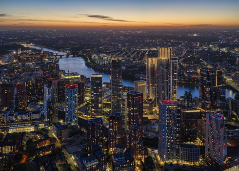 Aerial view of the modern Vauxhall skyline with illuminated skyscrapers the River Thames winding through the city and urban infrastructure at dusk in London England United Kingdom.