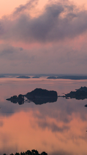 Aerial view of Oro Fortress Island surrounded by calm waters and forested islands under a soft pink sky at sunset in Oro Varsinais Suomi Finland. Aerial view of Oro Fortress Island surrounded by calm waters and forested islands under a soft pink sky at sunset in Oro Varsinais Suomi Finland.