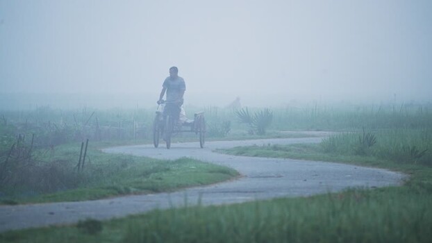 View of a man riding a rickshaw on a foggy road in Bangladesh.