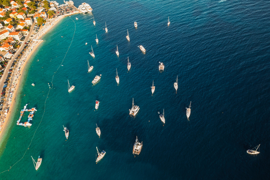 Aerial view of Primosten featuring numerous sailboats and yachts anchored in the clear turquoise waters of the Adriatic Sea along the coastline of Primosten Sibenik Knin County Croatia. Aerial view of Primosten featuring numerous sailboats and yachts anchored in the clear turquoise waters of the Adriatic Sea along the coastline of Primosten Sibenik Knin County Croatia.