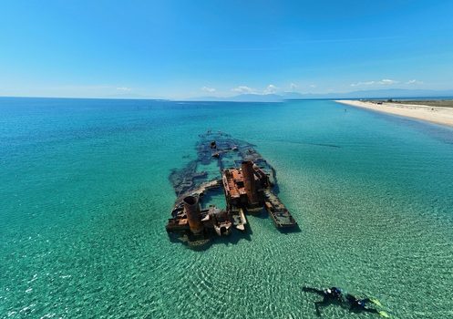 Aerial view of the rusty Shipwreck Epanomi in turquoise waters near a sandy beach with people swimming under a clear blue sky Epanomi Greece.