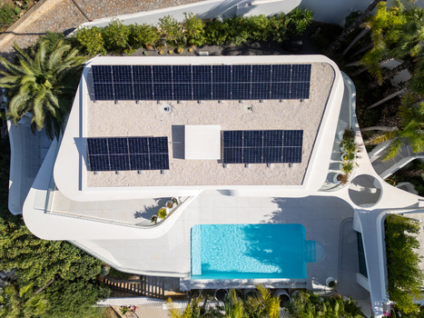 Aerial view of a modern house with solar panels on the roof and a turquoise swimming pool surrounded by lush greenery in Moraira Valencian Community Spain.