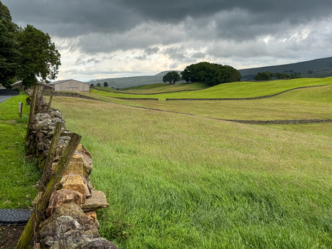 View of rolling green pastures and traditional dry stone walls under a dramatic cloudy sky in the Yorkshire Dales Hawes England United Kingdom. View of rolling green pastures and traditional dry stone walls under a dramatic cloudy sky in the Yorkshire Dales Hawes England United Kingdom.