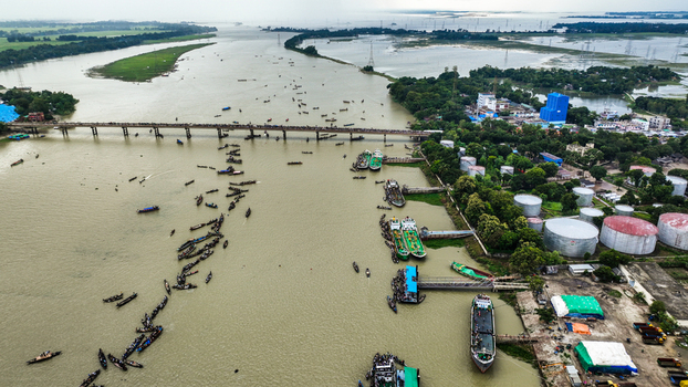 Baghabari Rajshahi Division Bangladesh 20 August 2022 Aerial view of the Baghabari river port with numerous boats industrial storage tanks and a bridge crossing the river.