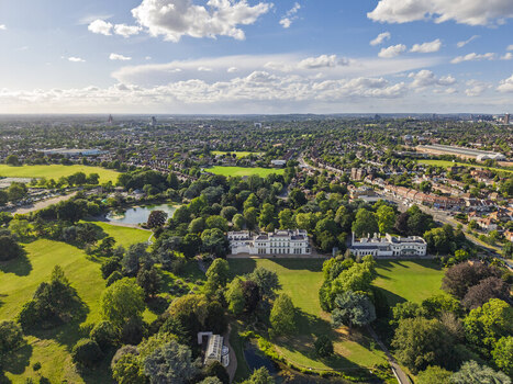 Aerial view of Gunnersbury Park featuring its historic mansion expansive green lawns mature trees and a small lake set within the urban landscape of London England United Kingdom. Aerial view of Gunnersbury Park featuring its historic mansion expansive green lawns mature trees and a small lake set within the urban landscape of London England United Kingdom.
