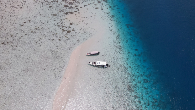 Aerial view of two boats anchored on a pristine white sandbar surrounded by shallow turquoise water and deep blue sea in Raja Ampat Southwest Papua Indonesia. Aerial view of two boats anchored on a pristine white sandbar surrounded by shallow turquoise water and deep blue sea in Raja Ampat Southwest Papua Indonesia.