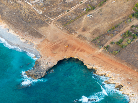 Aerial view of Riserva Naturale Orientata dello Zingaro featuring a small orange car parked on a dirt path near the turquoise waters and rocky coastline in San Vito Lo Capo Sicilia Italy. Aerial view of Riserva Naturale Orientata dello Zingaro featuring a small orange car parked on a dirt path near the turquoise waters and rocky coastline in San Vito Lo Capo Sicilia Italy.