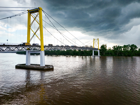 Aerial view of Barito Bridge spanning the Barito River with yellow suspension towers traffic on the deck and lush green riverbanks in Kecamatan Alalak Kalimantan Selatan Indonesia. Aerial view of Barito Bridge spanning the Barito River with yellow suspension towers traffic on the deck and lush green riverbanks in Kecamatan Alalak Kalimantan Selatan Indonesia.