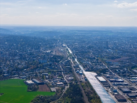 Aerial view of the glimmering canal cutting through the urban sprawl near the industrial zone and lush fields Sausheim Grand Est France.