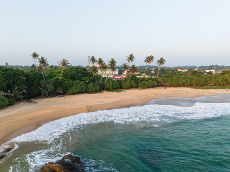 Aerial view of a sandy beach with turquoise waves crashing on the shore palm trees and people walking on the sand in Galle Southern Province Sri Lanka. Aerial view of a sandy beach with turquoise waves crashing on the shore palm trees and people walking on the sand in Galle Southern Province Sri Lanka.