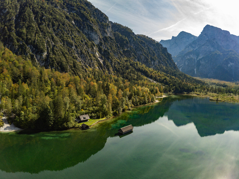 Aerial view of a mountain lake with a wooden boathouse and dense forest under a clear sky in Rottenbach Bayern Germany. Aerial view of a mountain lake with a wooden boathouse and dense forest under a clear sky in Rottenbach Bayern Germany.