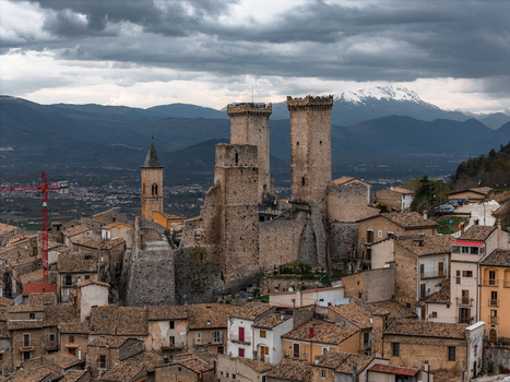 Aerial view of Castello Caldora and the historic stone houses of the medieval village under a dramatic cloudy sky with snow capped mountains in the background Pacentro Abruzzo Italy. Aerial view of Castello Caldora and the historic stone houses of the medieval village under a dramatic cloudy sky with snow capped mountains in the background Pacentro Abruzzo Italy.