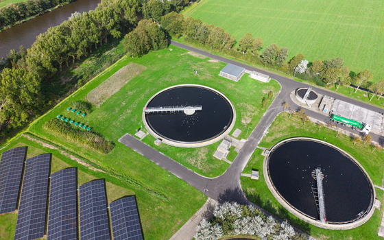 Aerial view of a water treatment plant featuring circular sedimentation tanks rows of solar panels and surrounding green fields in Schagerbrug Noord Holland Netherlands. Aerial view of a water treatment plant featuring circular sedimentation tanks rows of solar panels and surrounding green fields in Schagerbrug Noord Holland Netherlands.