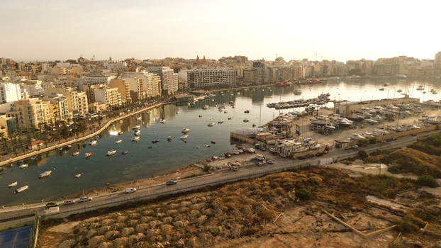 Aerial view of the marina in Msida with numerous boats moored in the harbor surrounded by urban buildings and coastal roads under the warm light in Malta. Aerial view of the marina in Msida with numerous boats moored in the harbor surrounded by urban buildings and coastal roads under the warm light in Malta.