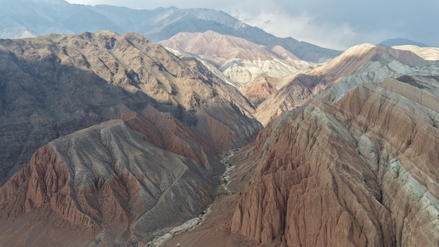 Aerial view of the rugged mountainous landscape of Song Kul with deep valleys and layered rock formations in Naryn Region Kyrgyzstan. Aerial view of the rugged mountainous landscape of Song Kul with deep valleys and layered rock formations in Naryn Region Kyrgyzstan.