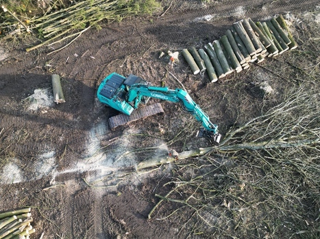 Netherlands 06 July 2026 Aerial view of an excavator working in a forest clearing with stacked logs and tire tracks visible on the muddy ground. Netherlands 06 July 2026 Aerial view of an excavator working in a forest clearing with stacked logs and tire tracks visible on the muddy ground.