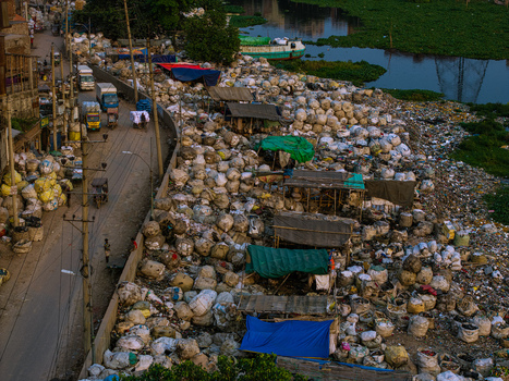 Aerial view of the Buriganga River bank filled with thousands of recycling bags and makeshift shelters under colorful tarps in Keraniganj Dhaka Division Bangladesh. Aerial view of the Buriganga River bank filled with thousands of recycling bags and makeshift shelters under colorful tarps in Keraniganj Dhaka Division Bangladesh.