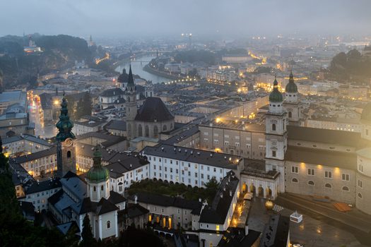 Aerial view of the historic city center of Salzburg with the illuminated Salzburg Cathedral winding river and traditional rooftops at dusk in Salzburg Salzburg Austria. Aerial view of the historic city center of Salzburg with the illuminated Salzburg Cathedral winding river and traditional rooftops at dusk in Salzburg Salzburg Austria.
