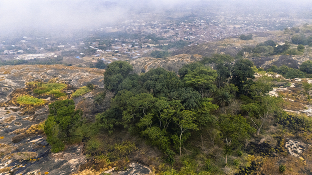 Aerial view of the lush green trees atop the rocky terrain contrast with the distant cityscape shrouded in mist IYAKE LAKE Oyo Nigeria. Aerial view of the lush green trees atop the rocky terrain contrast with the distant cityscape shrouded in mist IYAKE LAKE Oyo Nigeria.