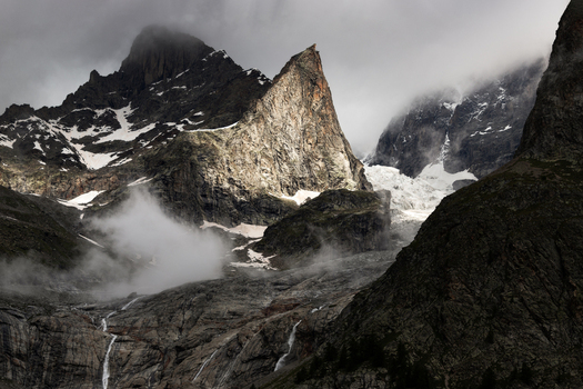 View of jagged mountain peaks with snow patches waterfalls and low clouds Aosta Valley Italy. View of jagged mountain peaks with snow patches waterfalls and low clouds Aosta Valley Italy.