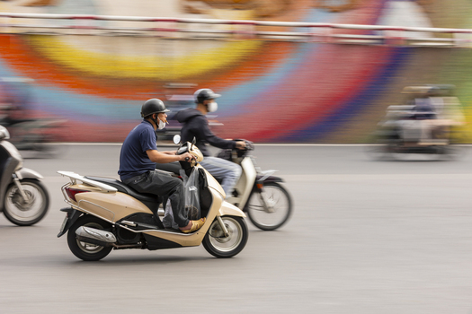 View of motorcyclists riding scooters along the Ceramic Mosaic Mural in the busy streets of Hanoi Ha Noi Vietnam.