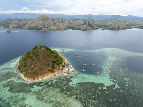 Aerial view of Pulau Kukusan with a small coastal village vibrant coral reefs and floating fish farming cages in the turquoise waters of Komodo East Nusa Tenggara Indonesia. Aerial view of Pulau Kukusan with a small coastal village vibrant coral reefs and floating fish farming cages in the turquoise waters of Komodo East Nusa Tenggara Indonesia.