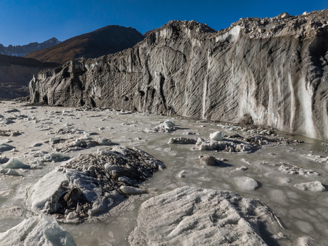 Aerial view of a massive glacier with textured ice formations and rocky debris under a clear blue sky in the Himalayas Nepal.
