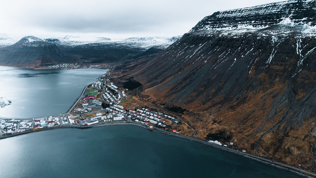 Aerial view of a city nestled between dark imposing mountains and the serene icy waters of a fjord Ísafjörður Iceland. Aerial view of a city nestled between dark imposing mountains and the serene icy waters of a fjord Ísafjörður Iceland.