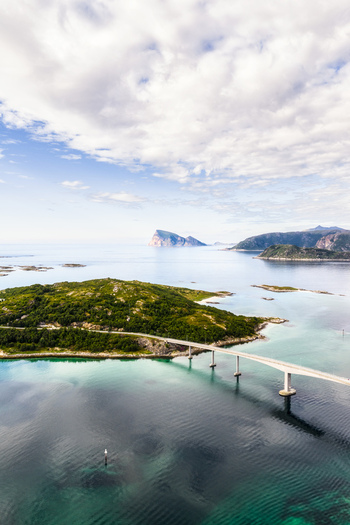 Aerial view of Sommaroy bridge connecting lush green islands over turquoise waters with distant mountains under a cloudy sky in Sommaroy Troms Norway. Aerial view of Sommaroy bridge connecting lush green islands over turquoise waters with distant mountains under a cloudy sky in Sommaroy Troms Norway.