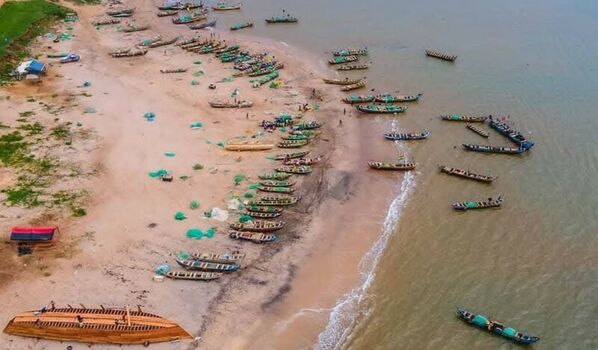 Aerial view of numerous wooden fishing boats and nets scattered along the sandy coastline with fishermen working on the shore in Ghana. Aerial view of numerous wooden fishing boats and nets scattered along the sandy coastline with fishermen working on the shore in Ghana.
