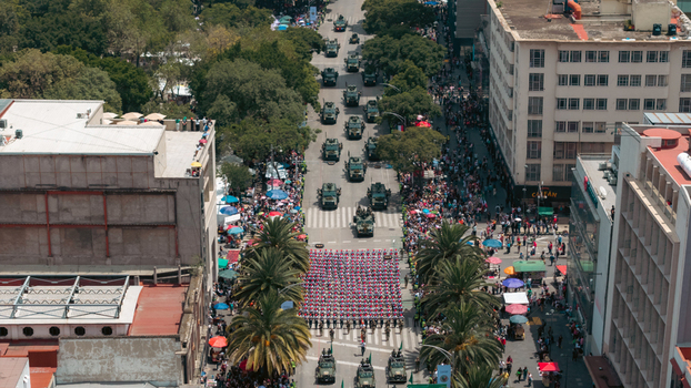 Aerial view of a military parade with soldiers marching in formation and military vehicles moving along a street lined with palm trees in Mexico City Mexico City Mexico.
