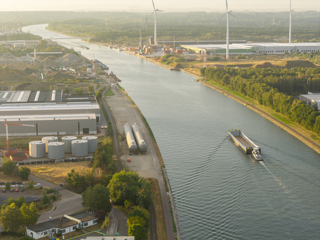 Aerial view of the Albert Canal with a barge navigating the waterway industrial facilities storage tanks and wind turbines in the golden hour light Genk Vlaanderen Belgium.